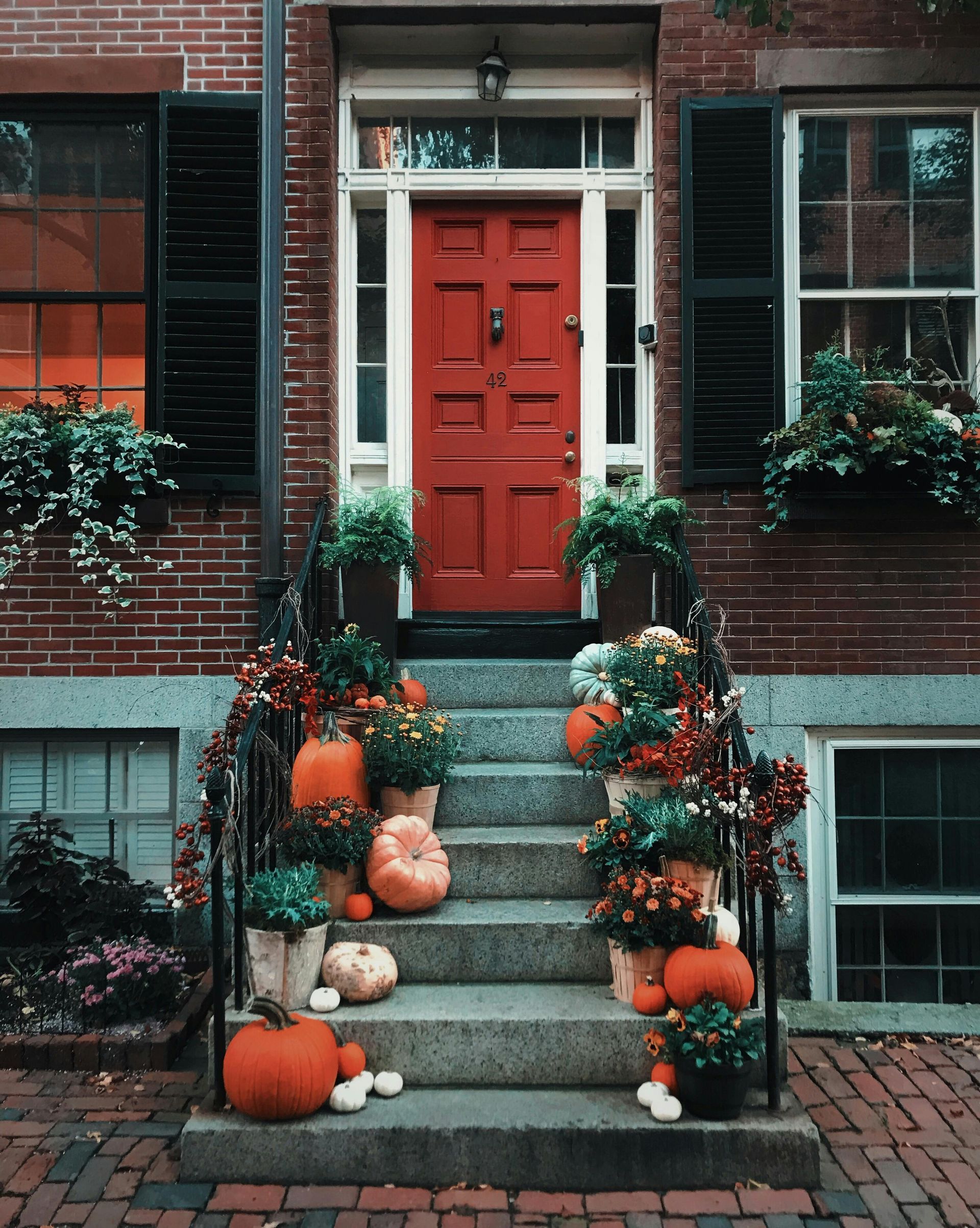 Red door decorated with pumpkins and flowers on a brick stoop.