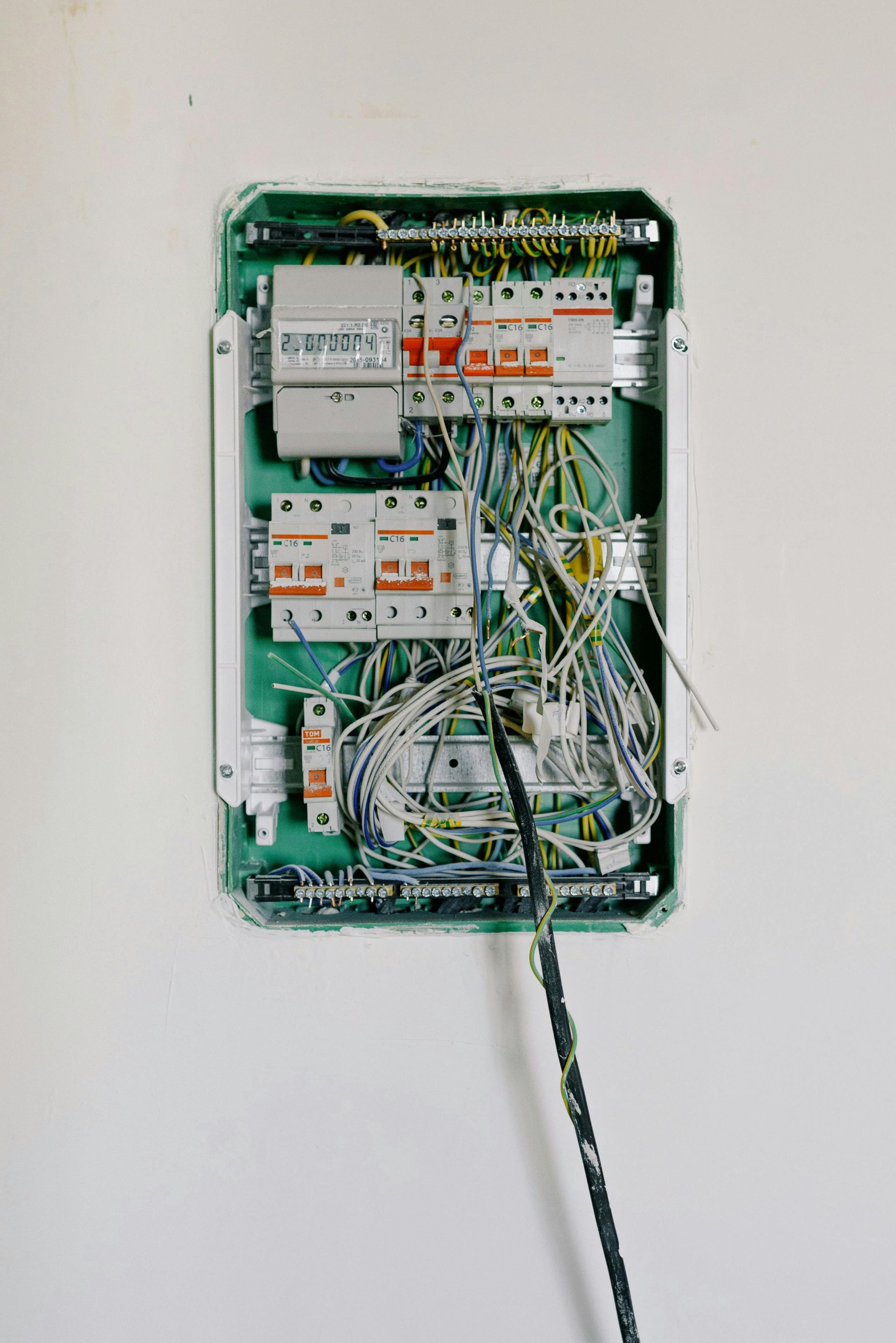 A very messy electrical box is hanging on a white wall.