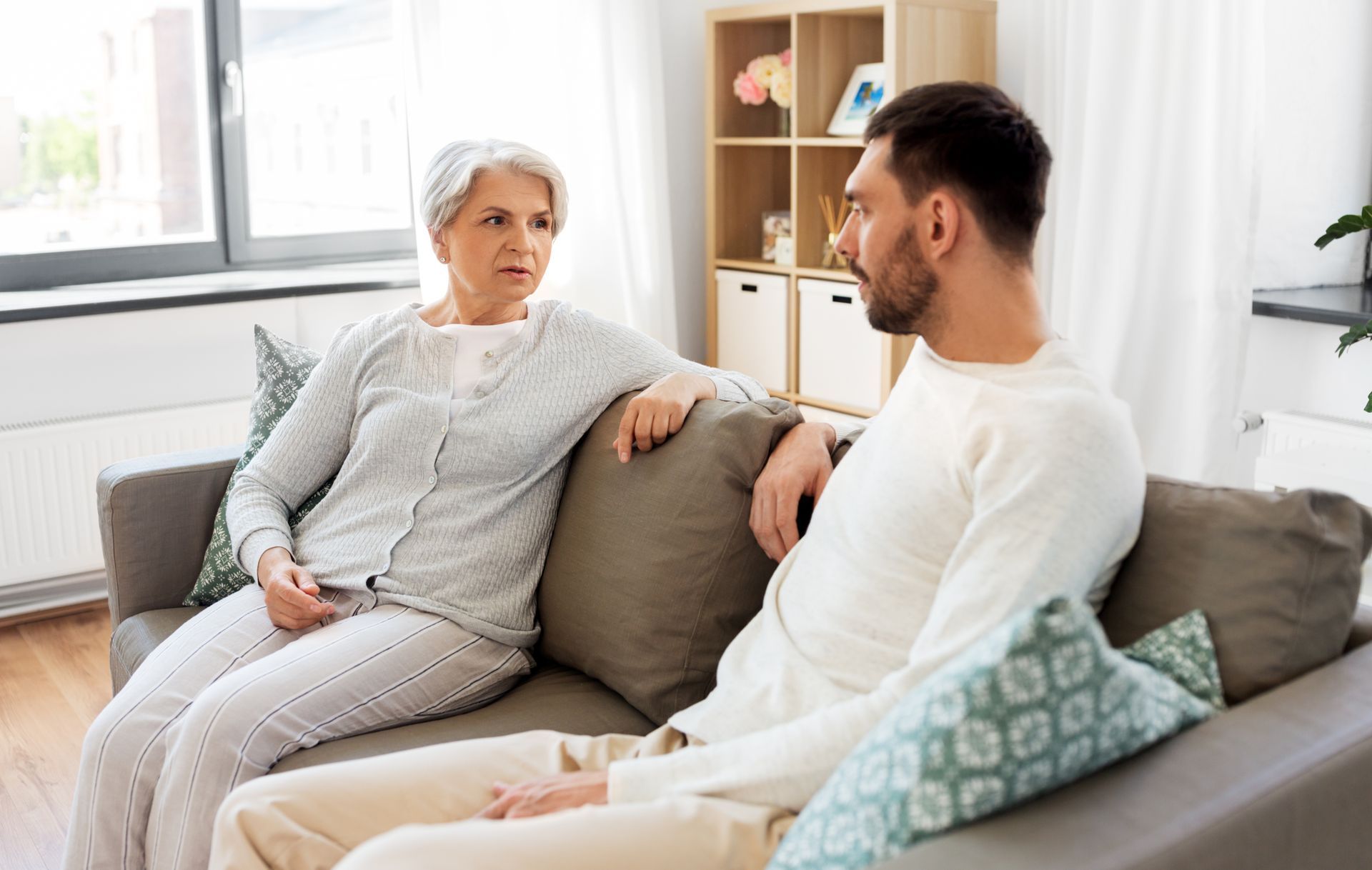 A senior mother is talking to her adult son on the couch at home.