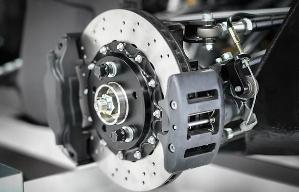Close-up of a car disc brake system with a perforated rotor, black calipers, and mounting hardware. | Scottsdale Protech
