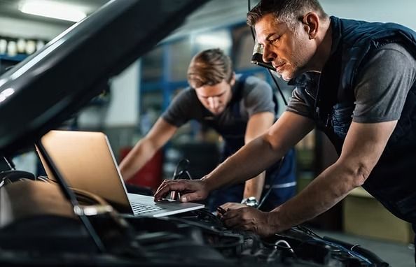 Two auto mechanics using a laptop to diagnose a car engine in a garage. | Scottsdale Protech
