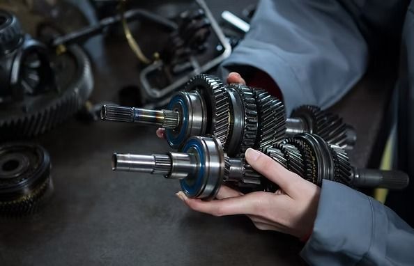 Mechanic holding a disassembled transmission, showing gears and shafts. Workshop setting. | Scottsdale Protech