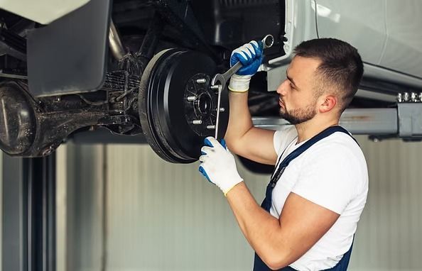 Mechanic working on a car's brakes, using a wrench in a repair shop. | Scottsdale Protech