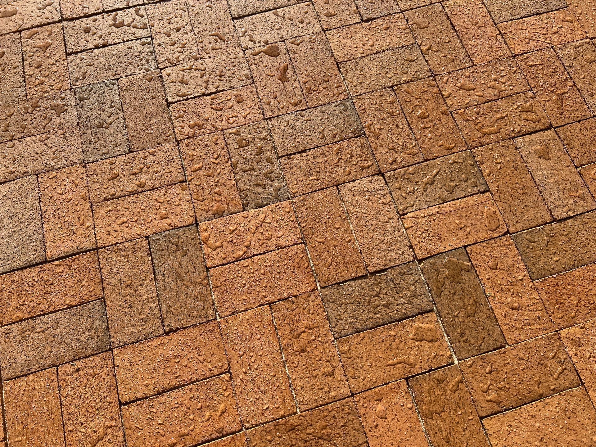 A close up of a brick patio with water drops on it.