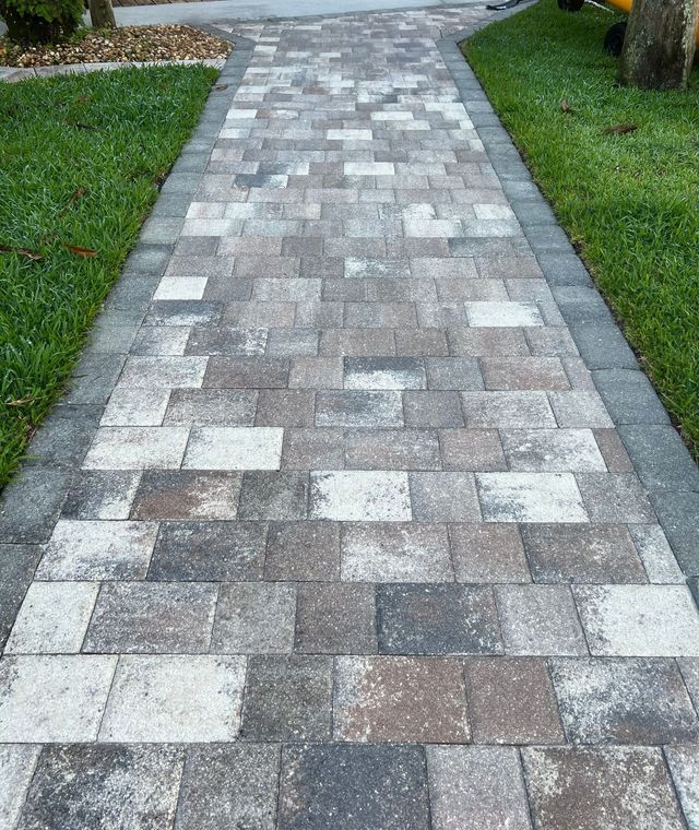 A brick paver walkway leading to a driveway with grass on both sides.