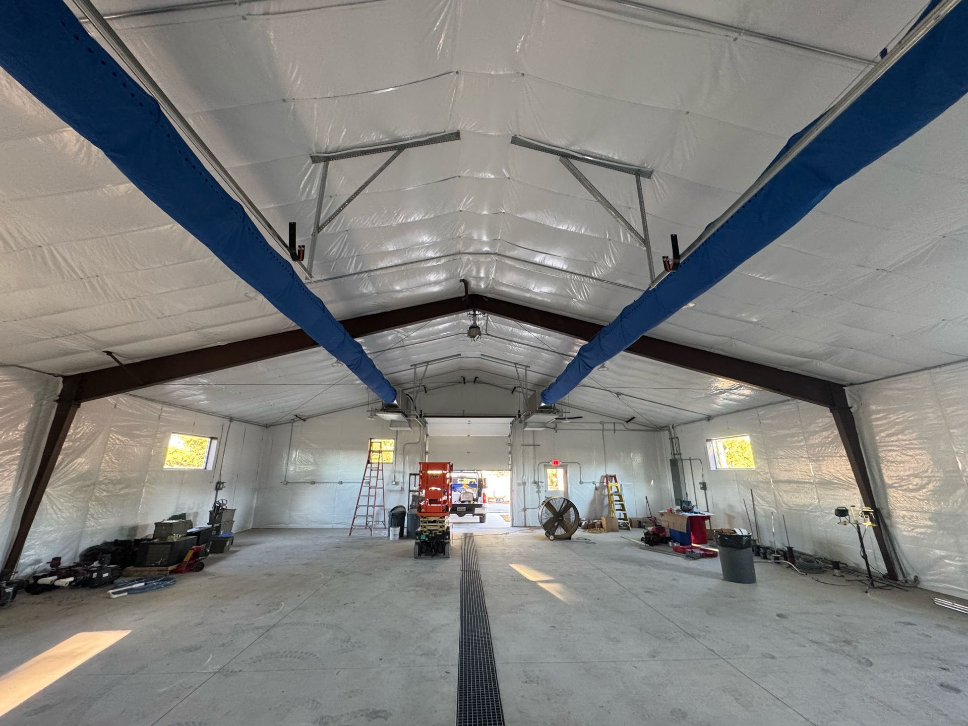Wide-angle view of a large, unfinished warehouse interior with white insulated walls, exposed steel beams, and blue ducts.