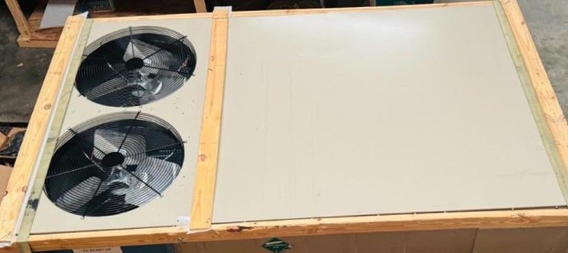 A horizontal view of a beige metal panel with two circular fan grilles, framed by wooden support beams on a flat surface.