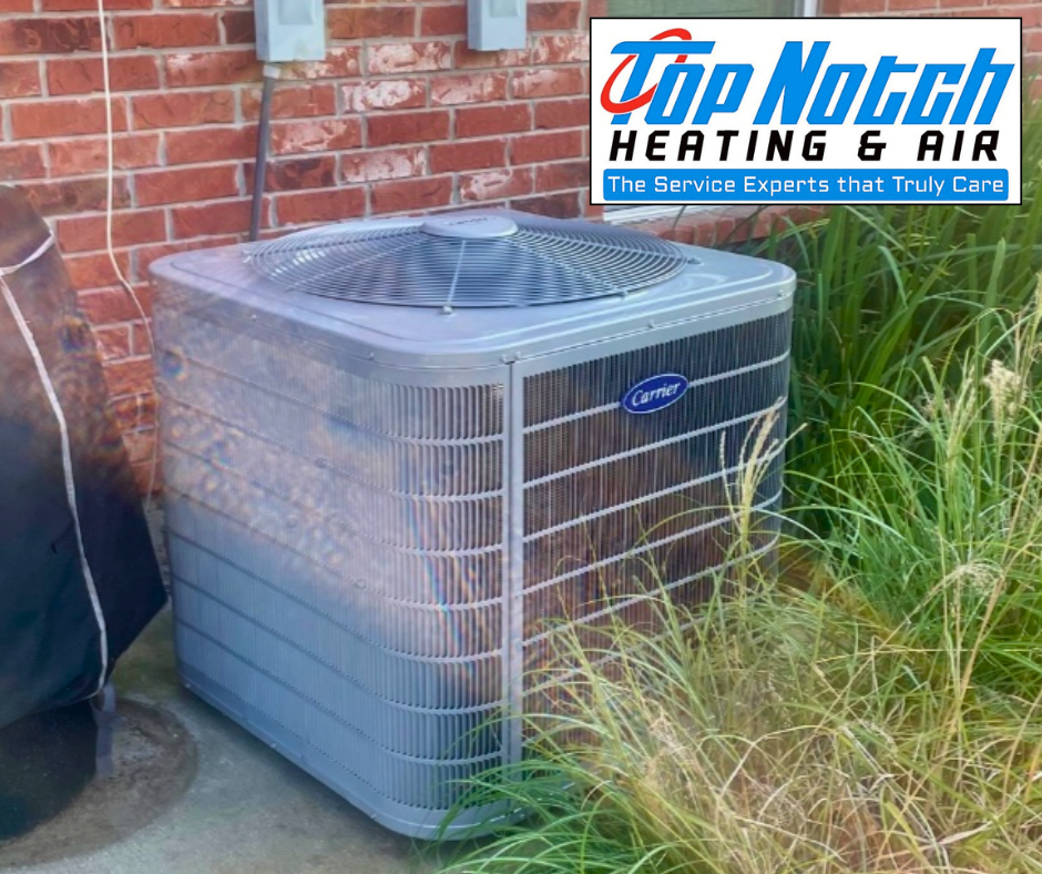 A Carrier outdoor HVAC unit next to a brick wall with a Top Notch Heating & Air logo overlay.