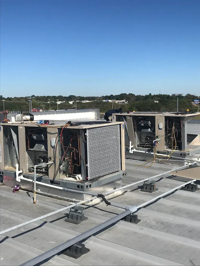 Two rooftop HVAC units undergo maintenance on a sunny day with exposed internal components and piping visible.