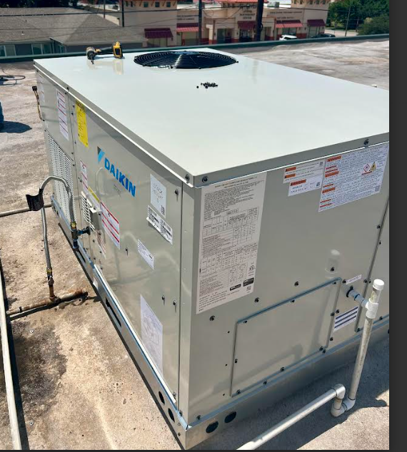 A beige Daikin rooftop HVAC unit sits on a flat building roof under bright sunlight.