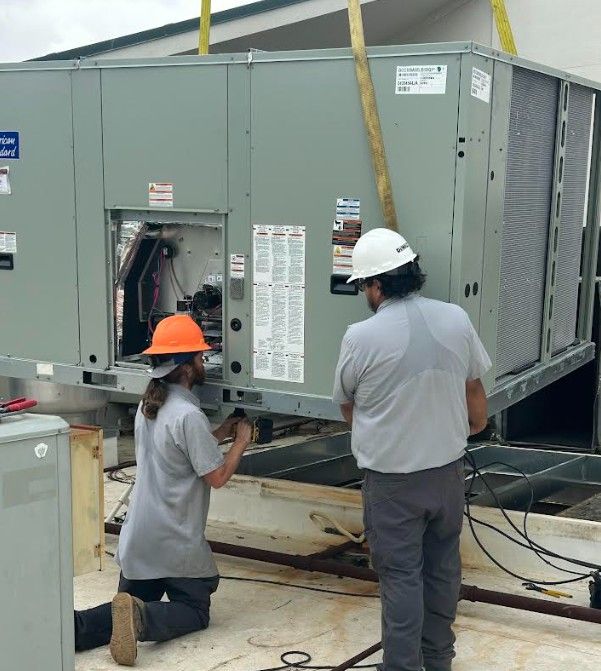 Man crouches, working on beige electrical equipment, under a blue umbrella, outdoors. Man crouches, working on beige electrical equipment, under a blue umbrella, outdoors.