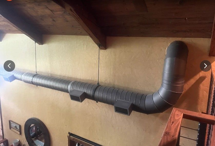 An exposed, gray industrial duct system mounted horizontally along a beige wall below a wooden ceiling.