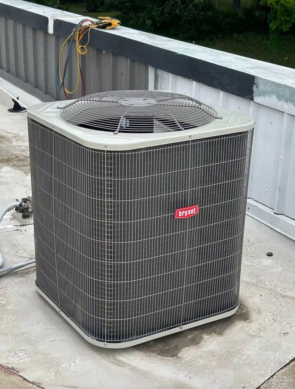 A square, light-colored Bryant HVAC condenser unit sits on a rooftop near a metal railing.