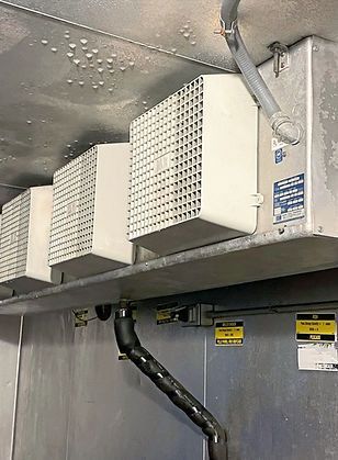 Three white rectangular vents mounted on a metal wall with a dark drain pipe. Three white rectangular vents mounted on a metal wall with a dark drain pipe.