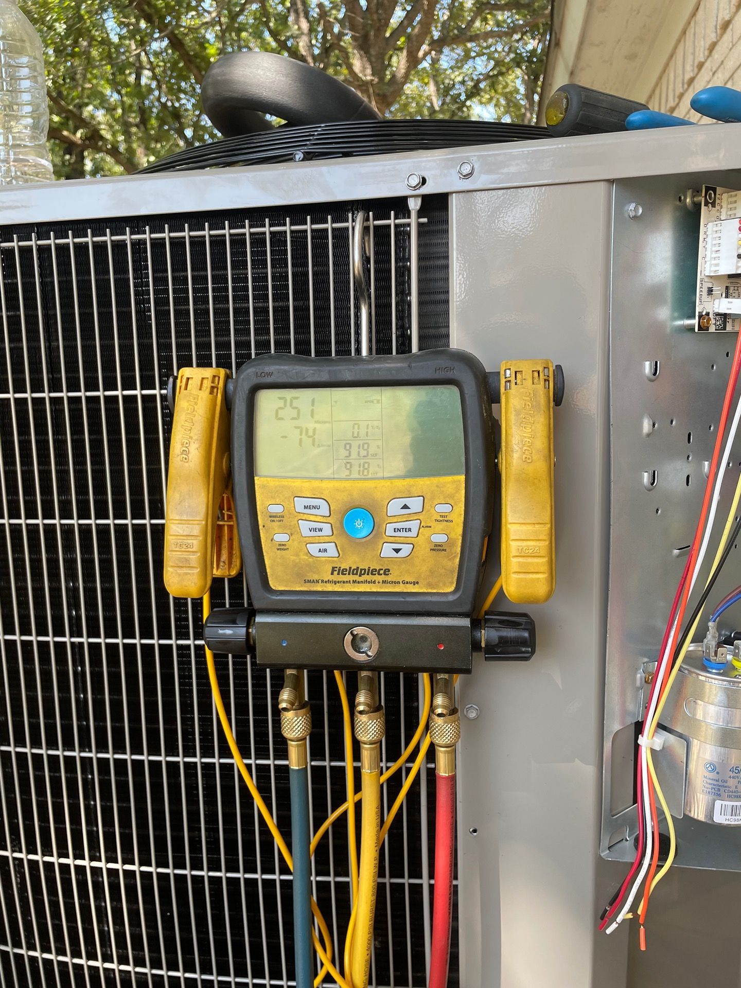 A digital manifold gauge set hooked up to an outdoor HVAC unit to monitor refrigerant pressures and temperatures.