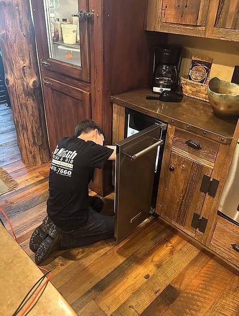 Person kneeling, working on small refrigerator in rustic kitchen. Person kneeling, working on small refrigerator in rustic kitchen.