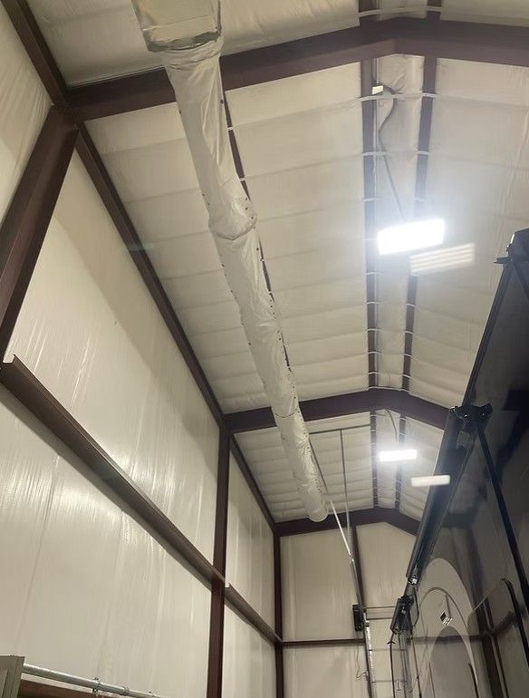 Interior of a high-ceilinged building with white insulated panels, metal beams, a fabric air duct, and overhead lights.