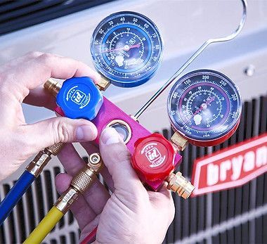 Hands using gauges to test an air conditioning unit; blue, yellow, and red hoses are attached.
