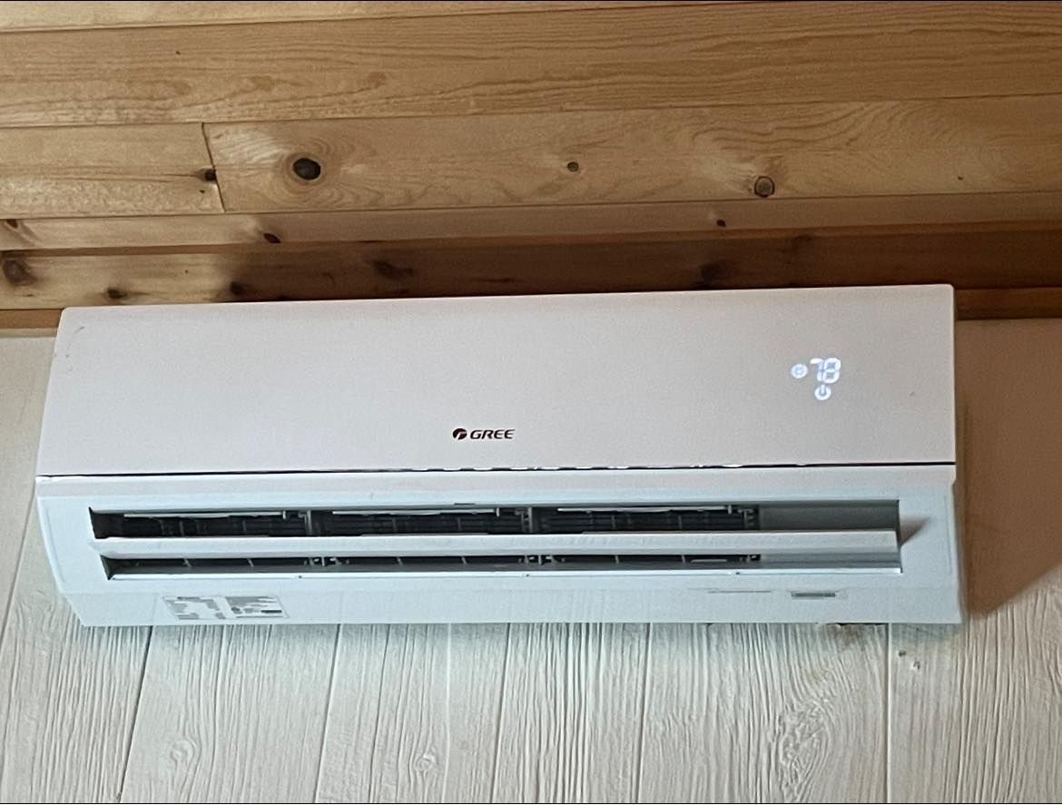 A white wall-mounted air conditioner unit is installed against a wood-paneled wall, displaying a temperature of 20°C.