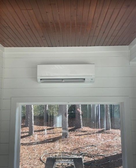 A white wall-mounted air conditioner unit installed on a white shiplap wall beneath a dark wood ceiling.