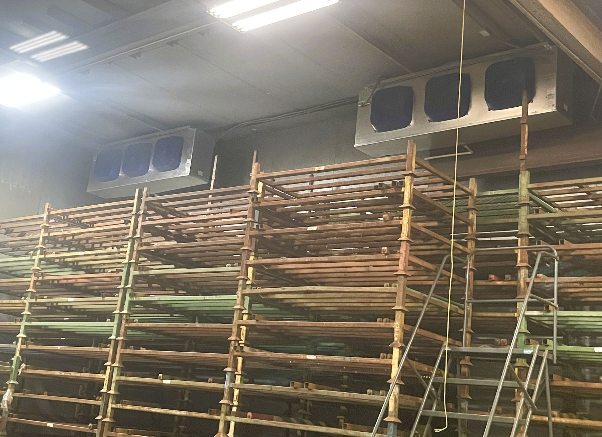 Industrial warehouse ceiling-mounted ventilation units above stacked metal shelving racks.