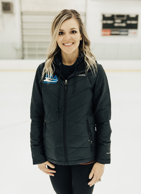 Woman in black jacket smiles, standing on ice rink.