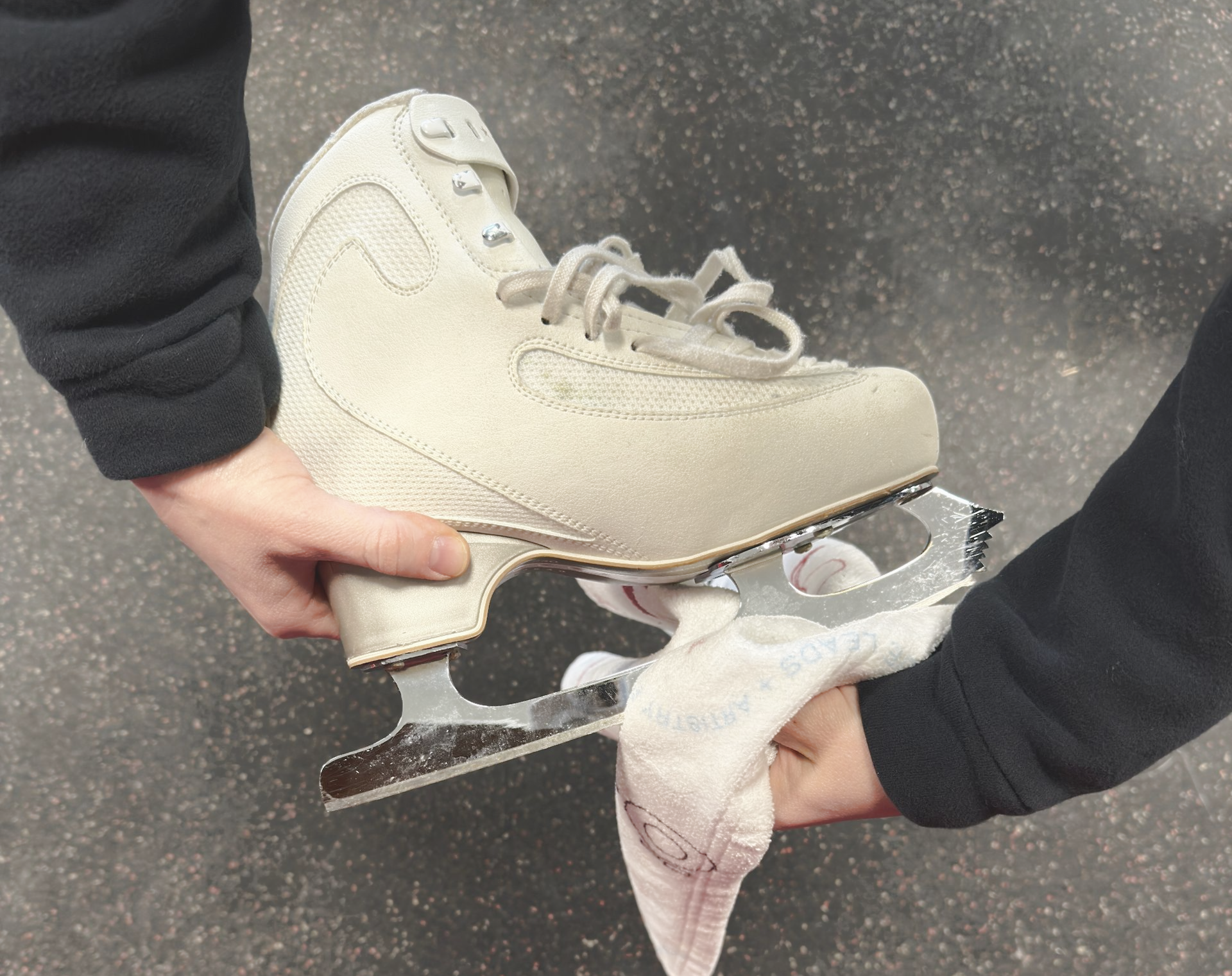 Person holding white ice skate, wiping blade with green cloth.