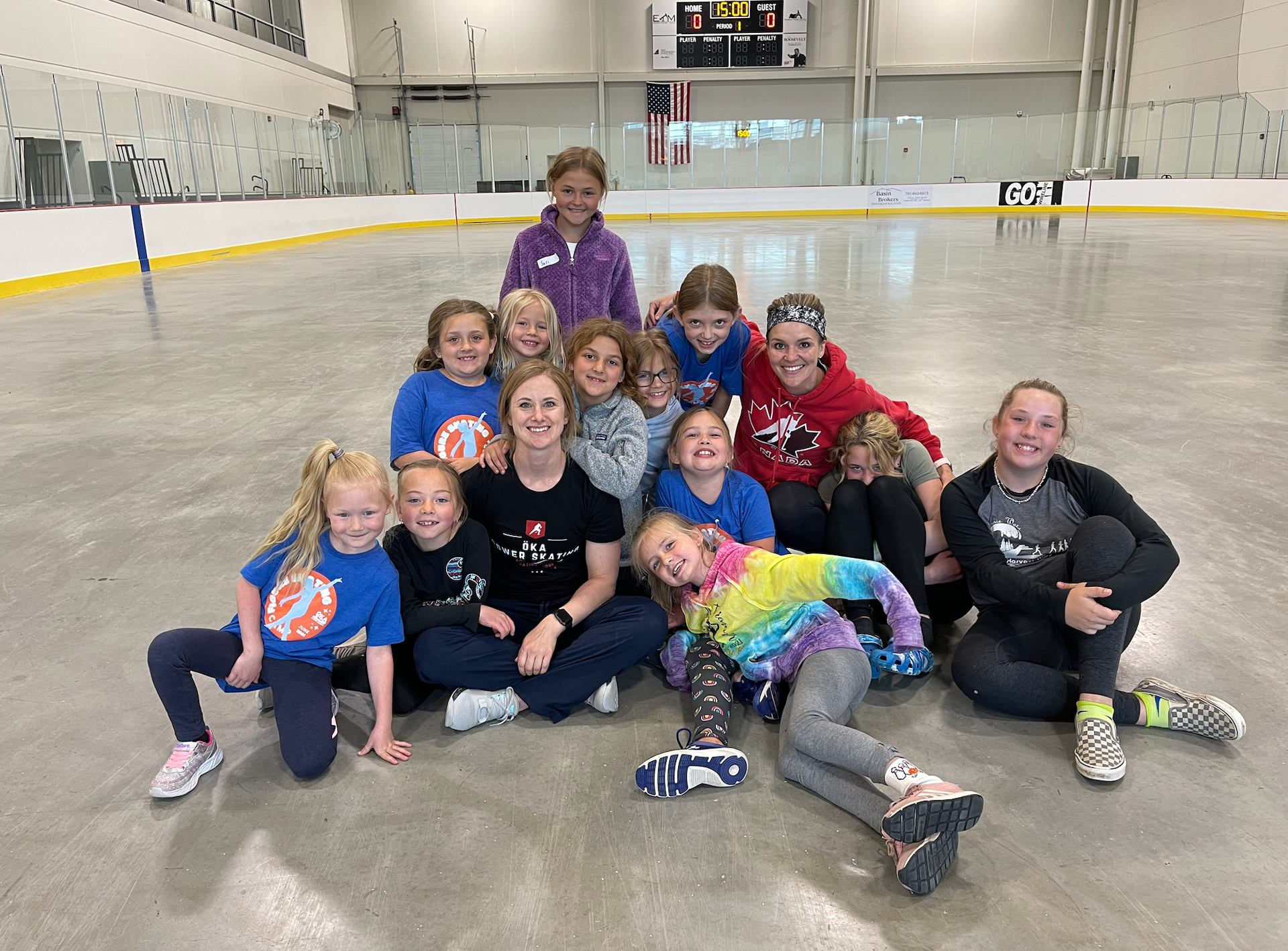 Young ice skaters in formation on a rink, wearing matching tops, gloves, and skates, posing.