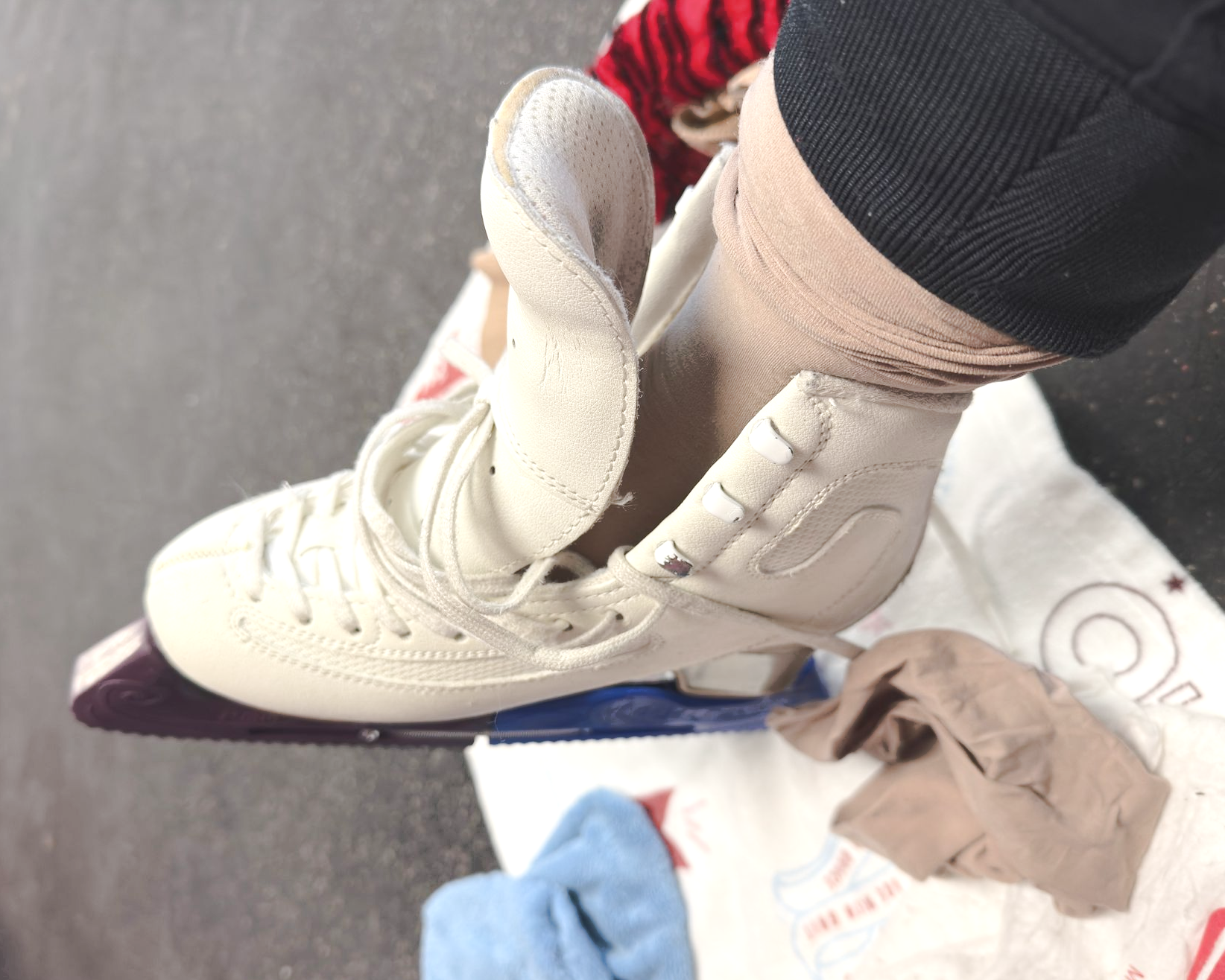 Cream lace-up sneaker on a leg in a gym or store interior, with red and black counters in the background