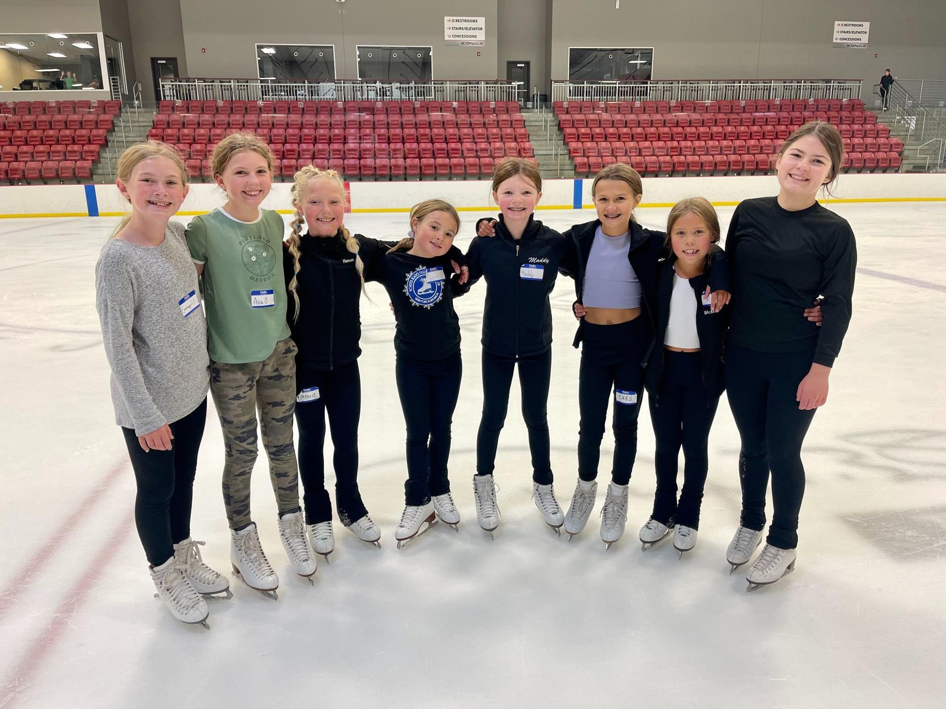 Group of children in ice skates pose on an ice rink, smiling and posing.