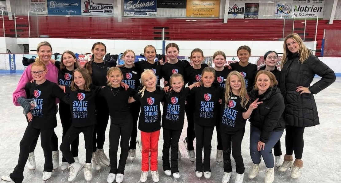 Group of ice skaters in black shirts pose on ice rink.