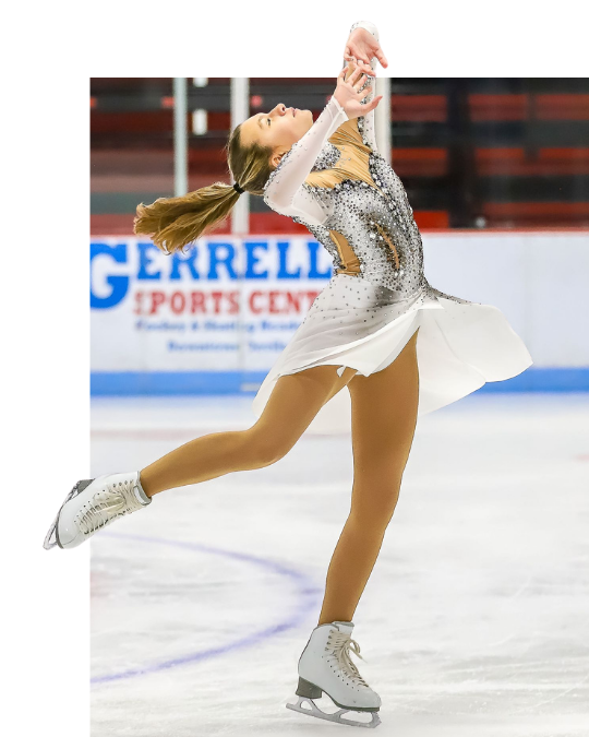 Young skater in yellow dress smiles on ice rink.