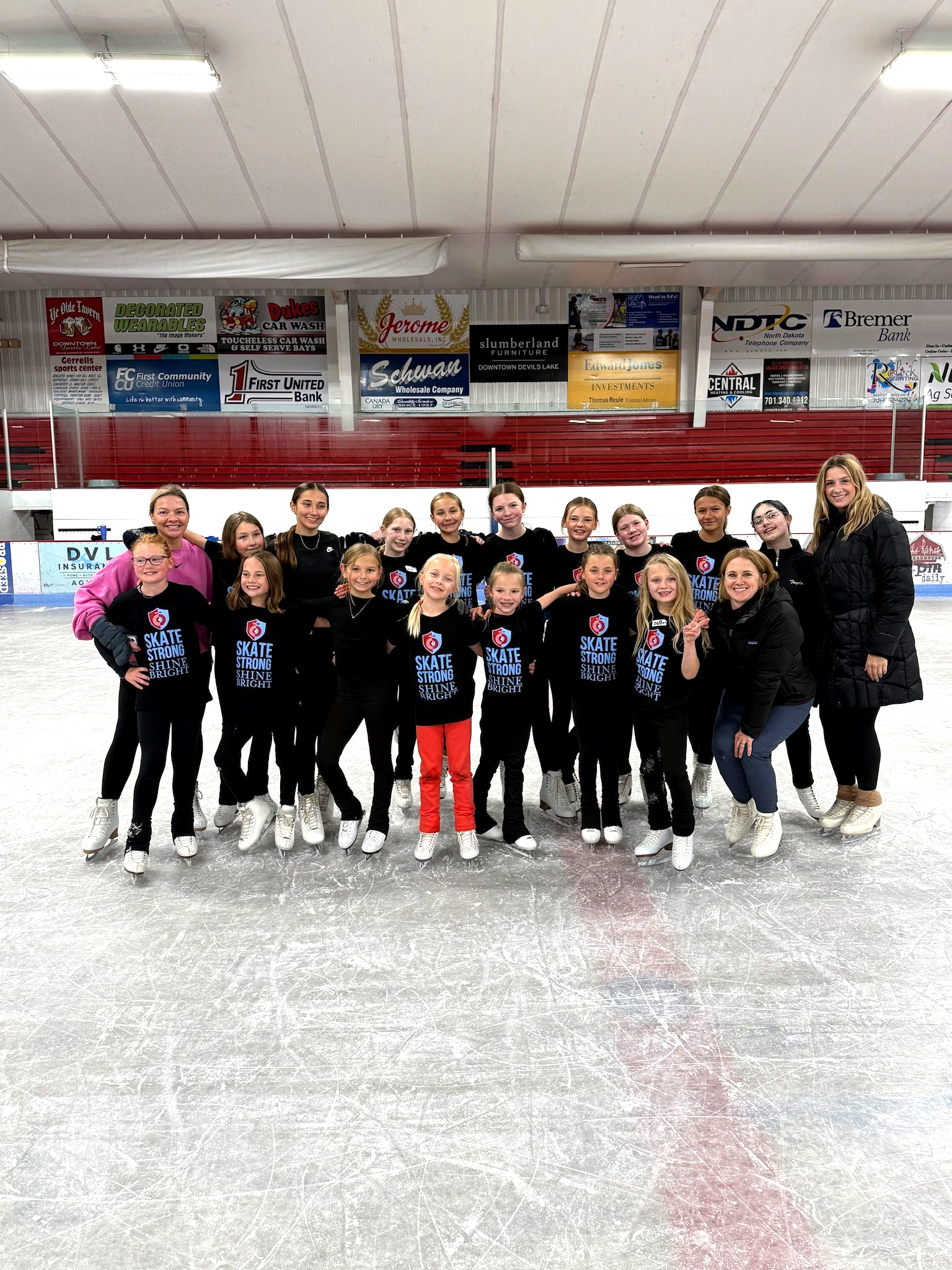Youth hockey team posing on an ice rink, wearing black jerseys with raised arms and smiles.