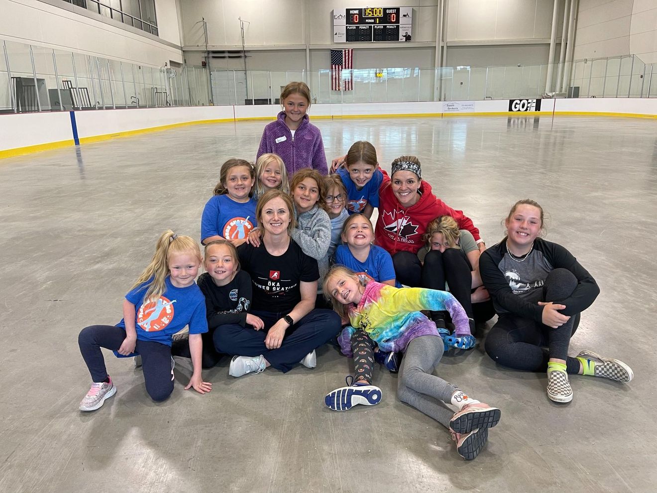 Group of children and adults pose on an ice rink. Some wearing hockey or sports apparel, smiling.