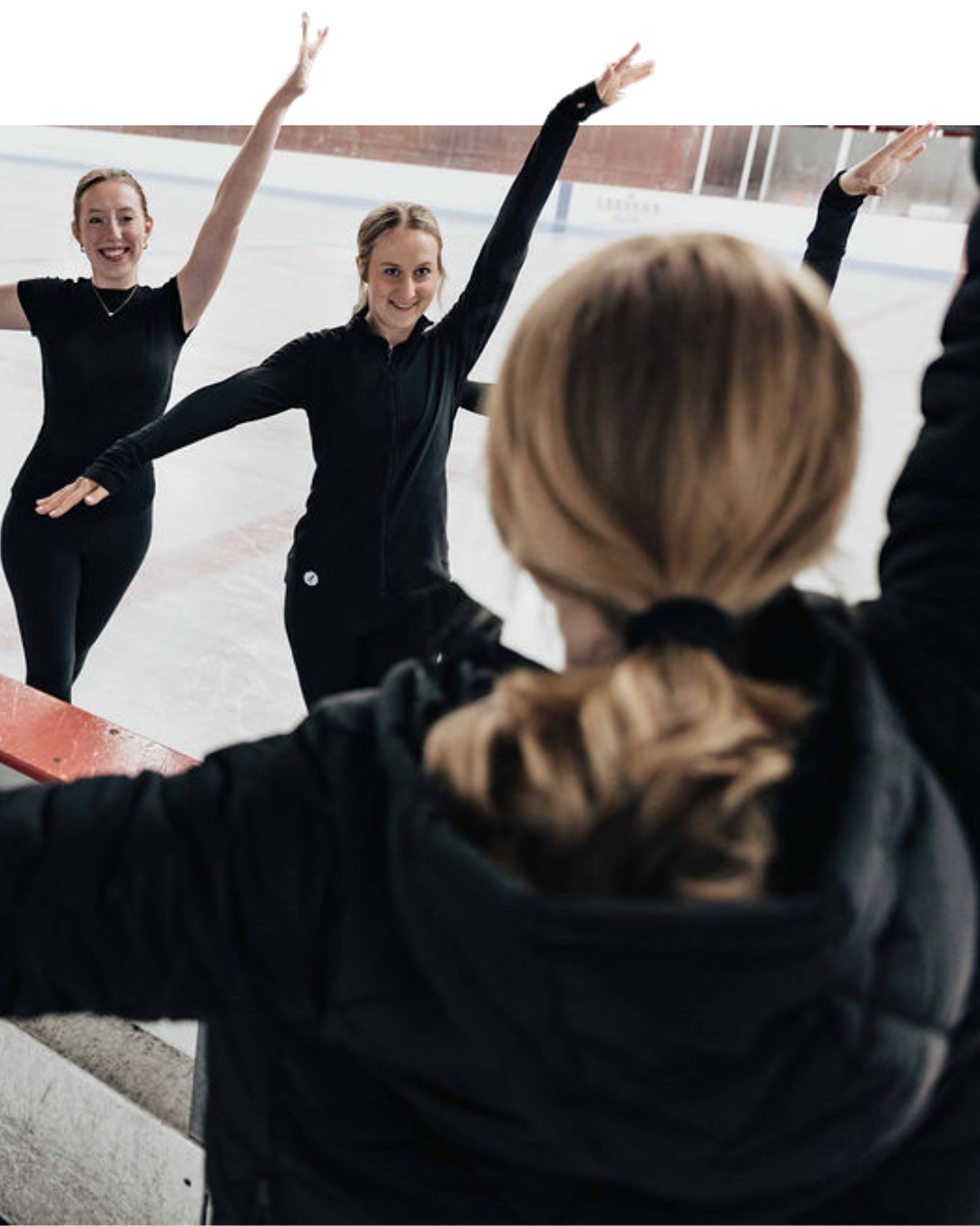 Three ice skaters in black outfits on a rink, arms raised.