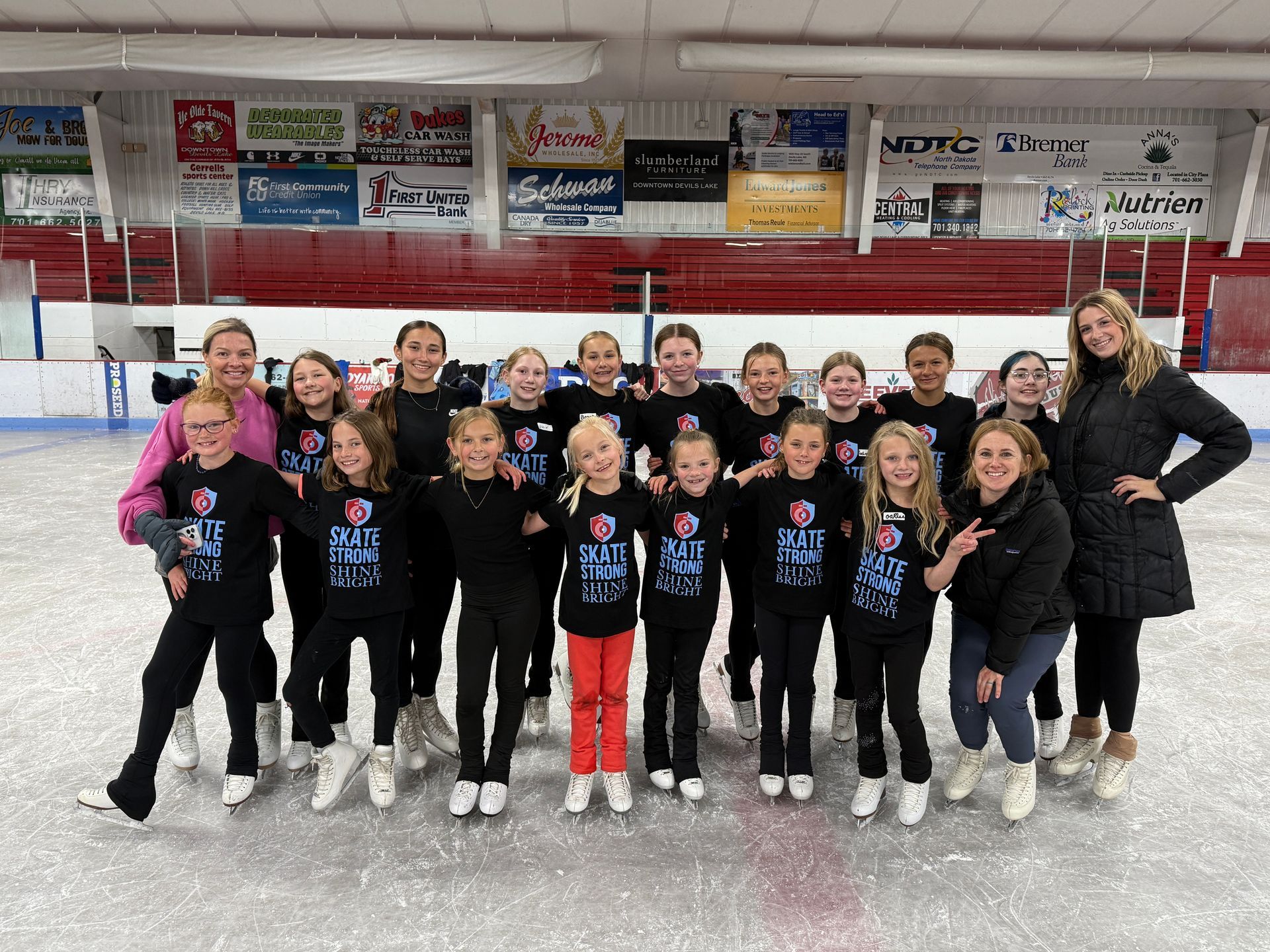 Woman on ice skates supporting another skating, balancing, holding pose. Arena backdrop.