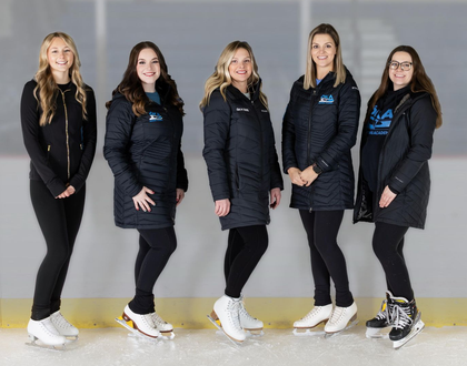 Five people on ice skates pose on an ice rink, all wearing black jackets and leggings.