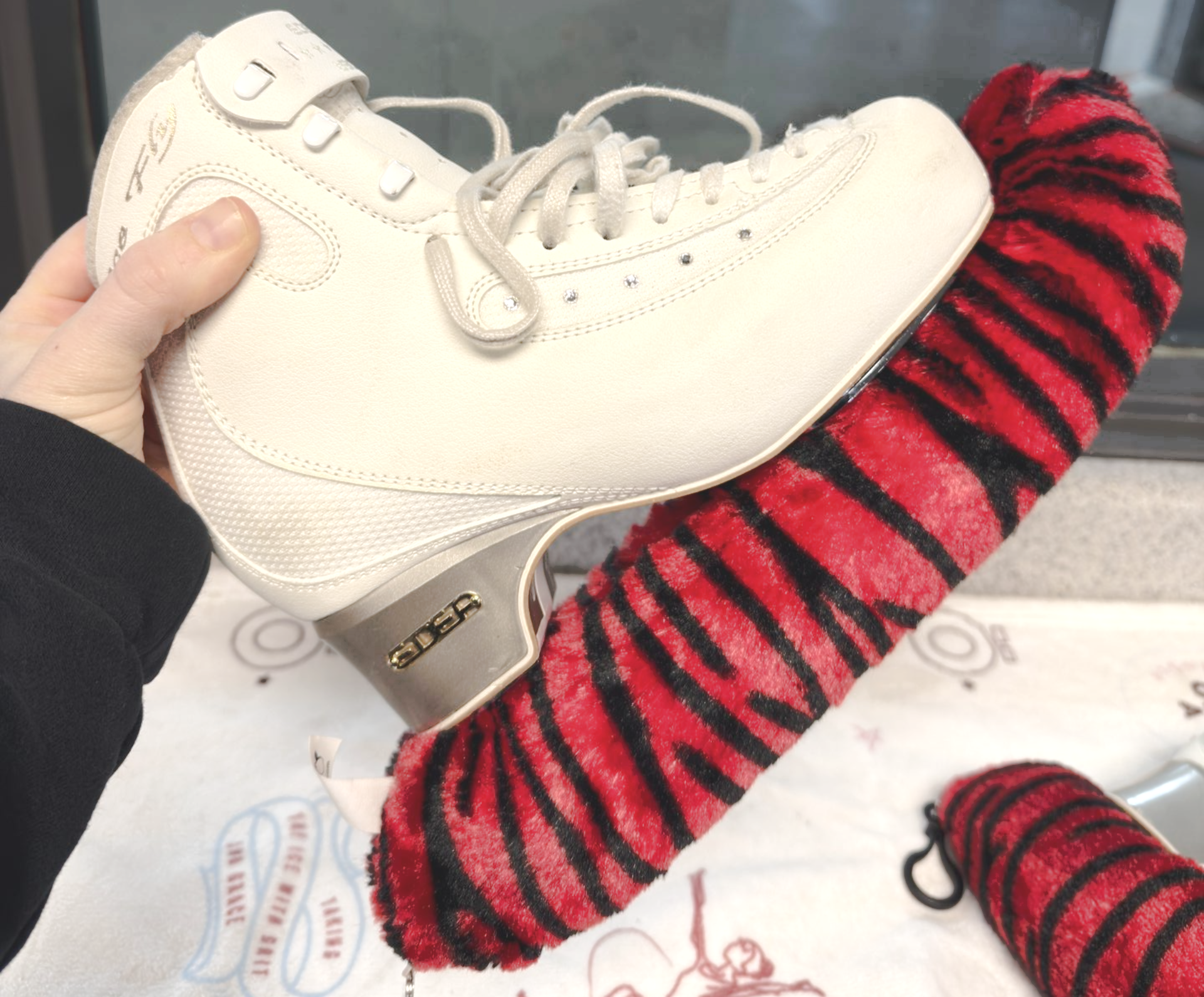 Person holding white ice skate, wiping blade with green cloth.