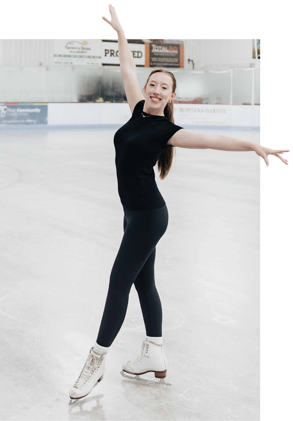 Figure skater on ice, arms outstretched, smiling. Black outfit, ice rink backdrop.