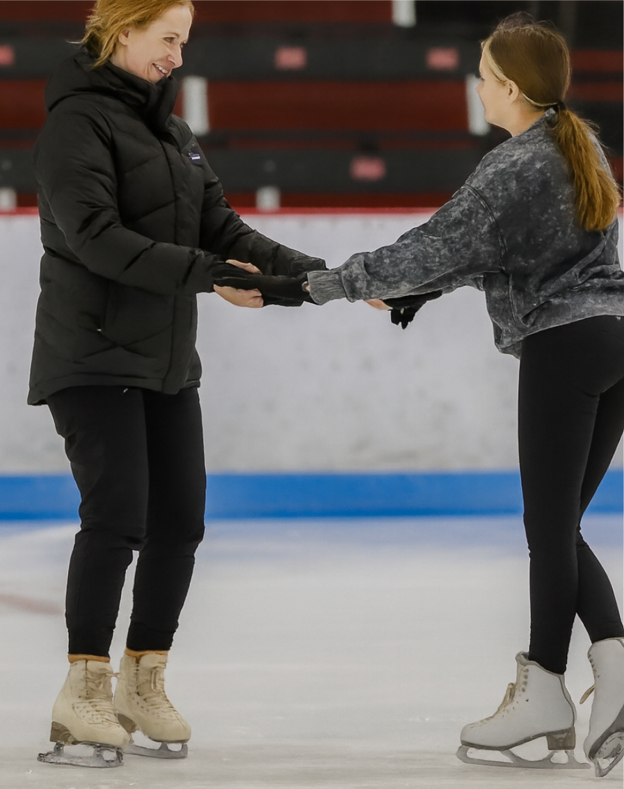 Two people ice skating, holding hands. One wears a black jacket, the other a gray sweatshirt.