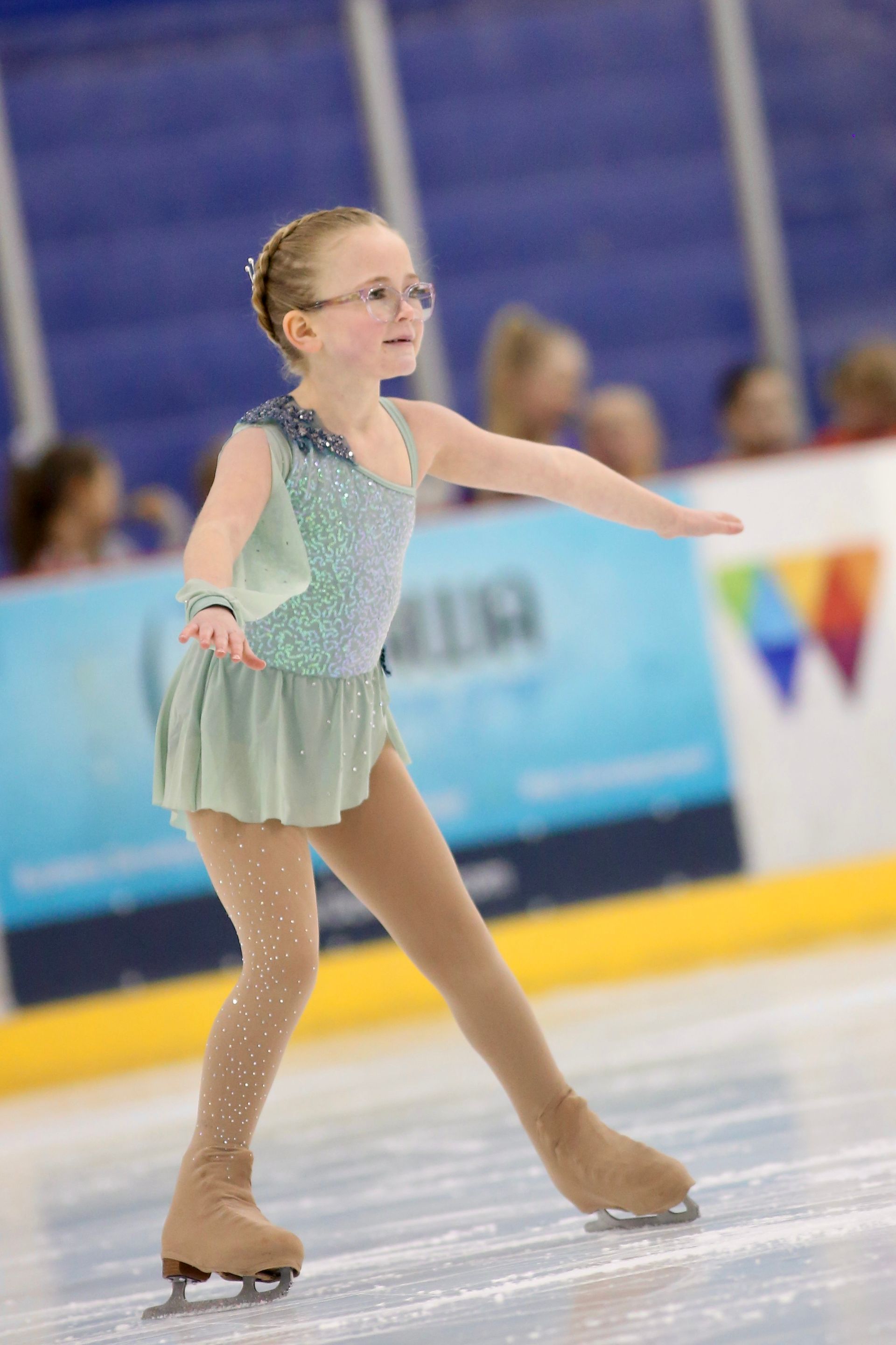 Figure skater in a blue dress performs a lunging pose on ice, pointing forward.