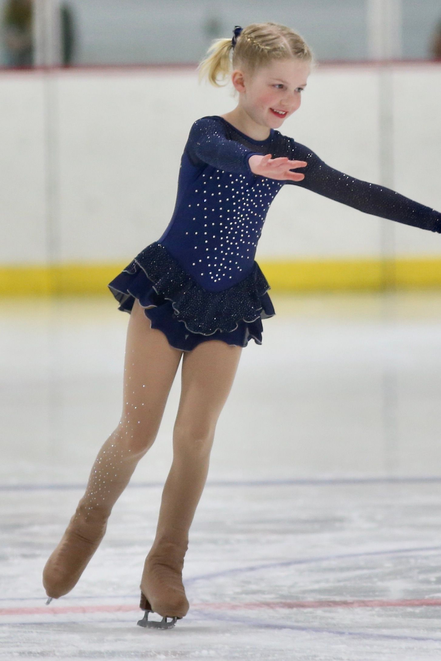Young figure skater in a navy dress with sparkles, on ice, smiling.