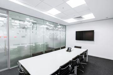 Modern conference room with a white table, black chairs, and a glass-walled partition, set against a plain white wall.