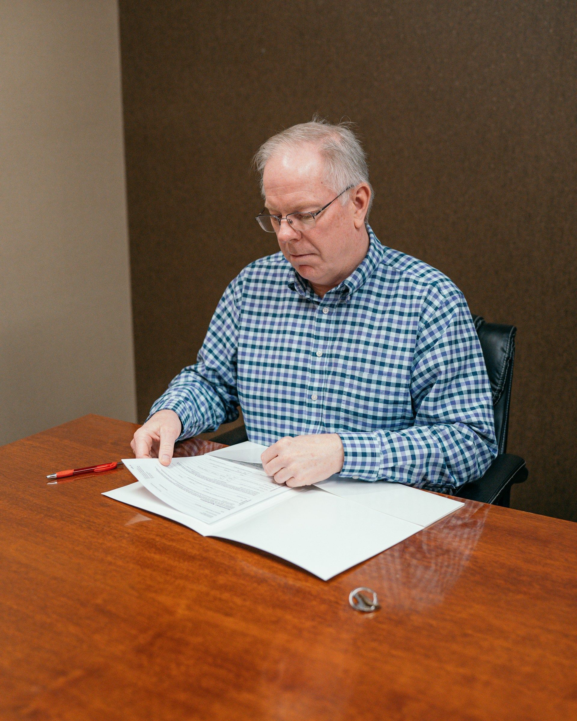 An elderly couple examines paperwork together at a table, one pointing while the other types on a laptop.