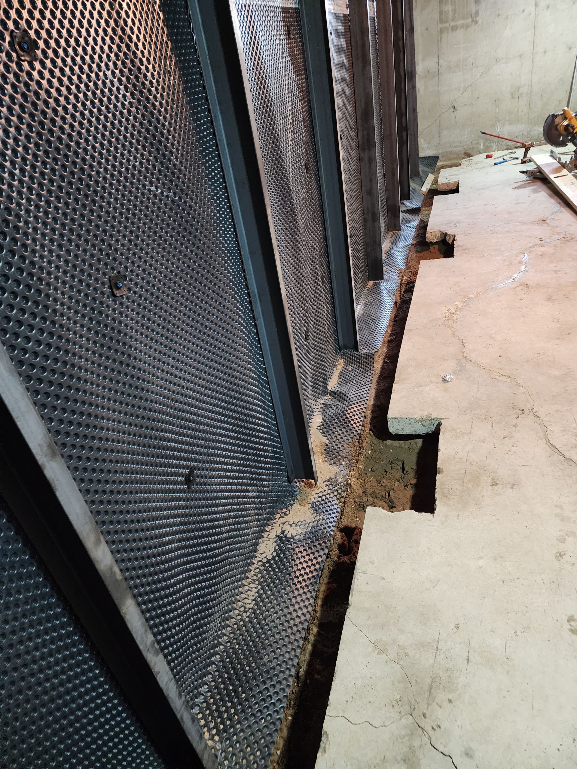 Black drainage membrane installed on a concrete wall. A trench runs along the floor.