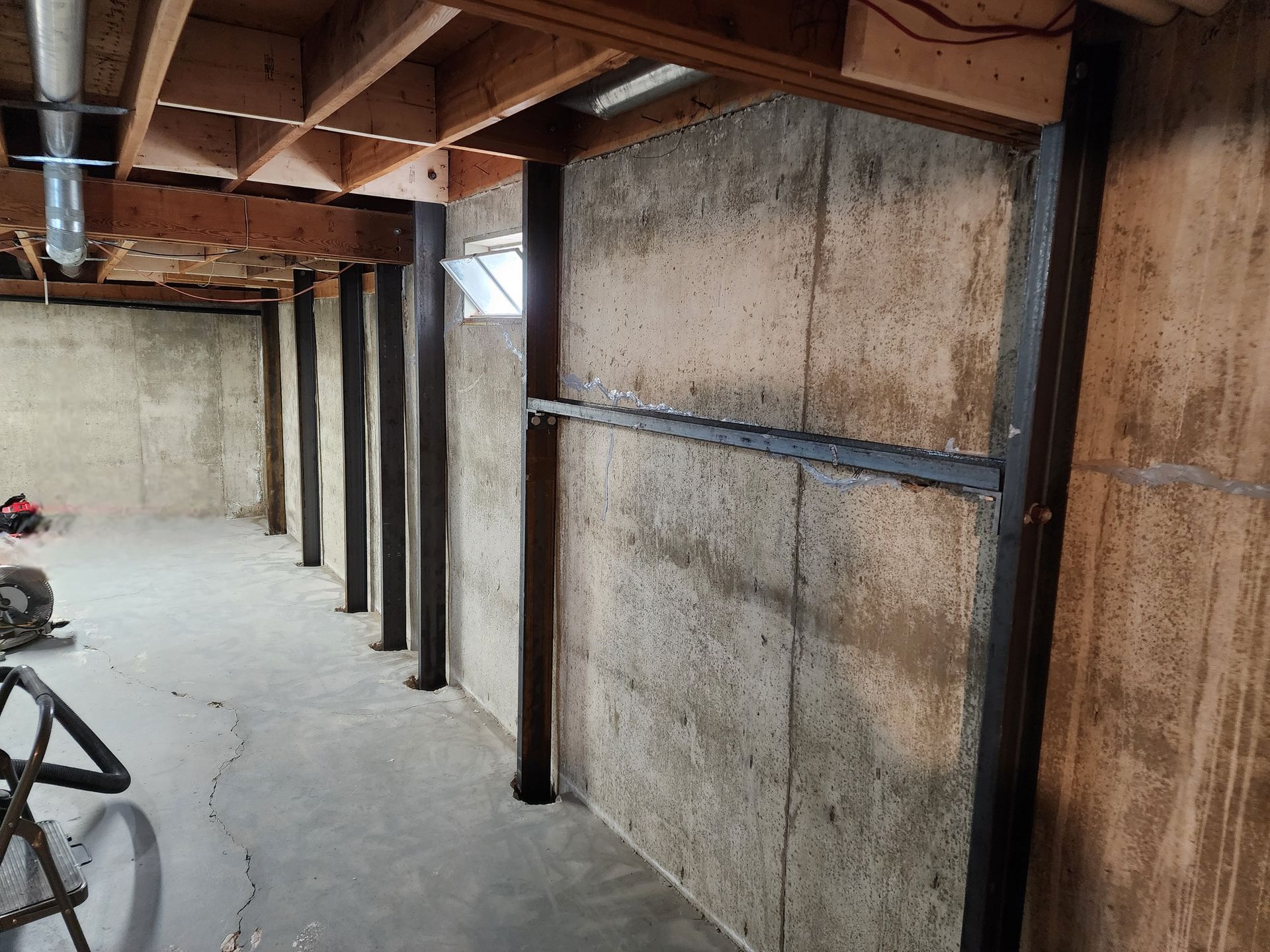 Basement with steel beams supporting a concrete wall. Wooden joists overhead