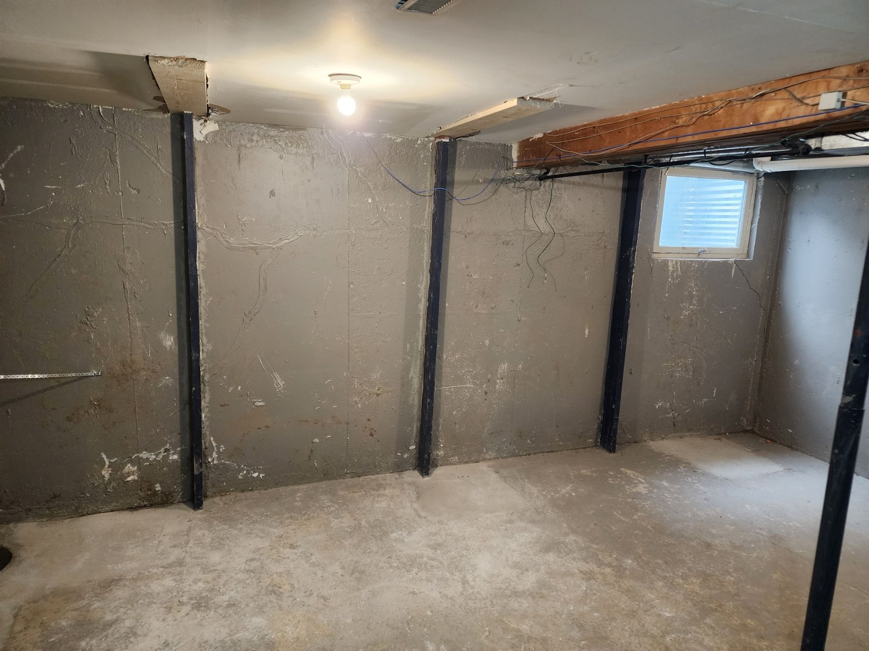Basement interior with structural supports and concrete walls.