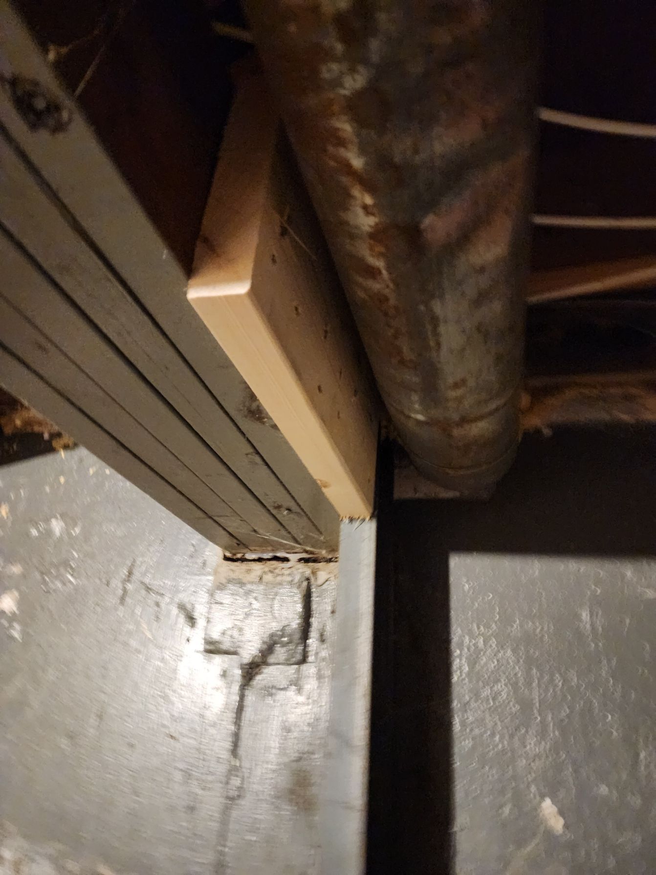 Wooden beam support added near a duct in a concrete-floored basement.