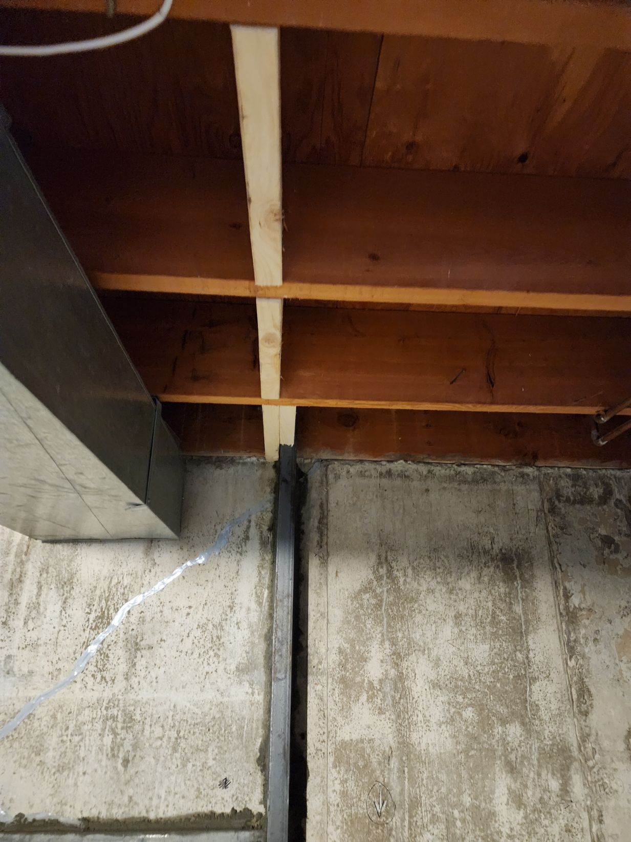Basement ceiling with wood beams and a vertical support beam against a concrete wall.