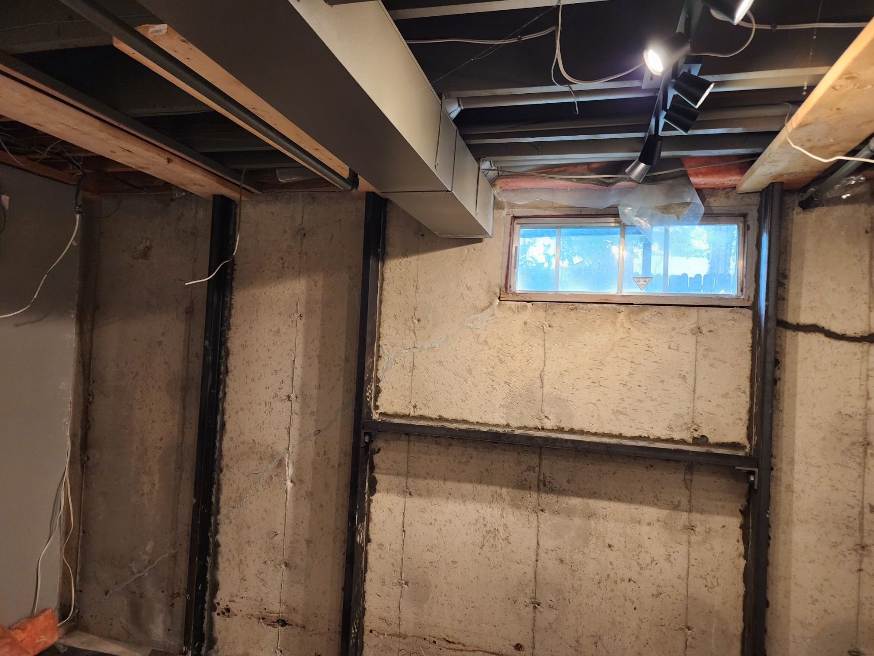 Basement with concrete walls, window, steel beams, and wooden supports,